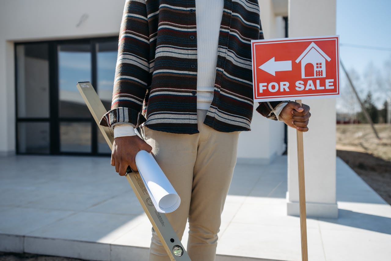 A real estate agent stands outside with a for sale sign and rolled blueprint, suggesting a property for sale.